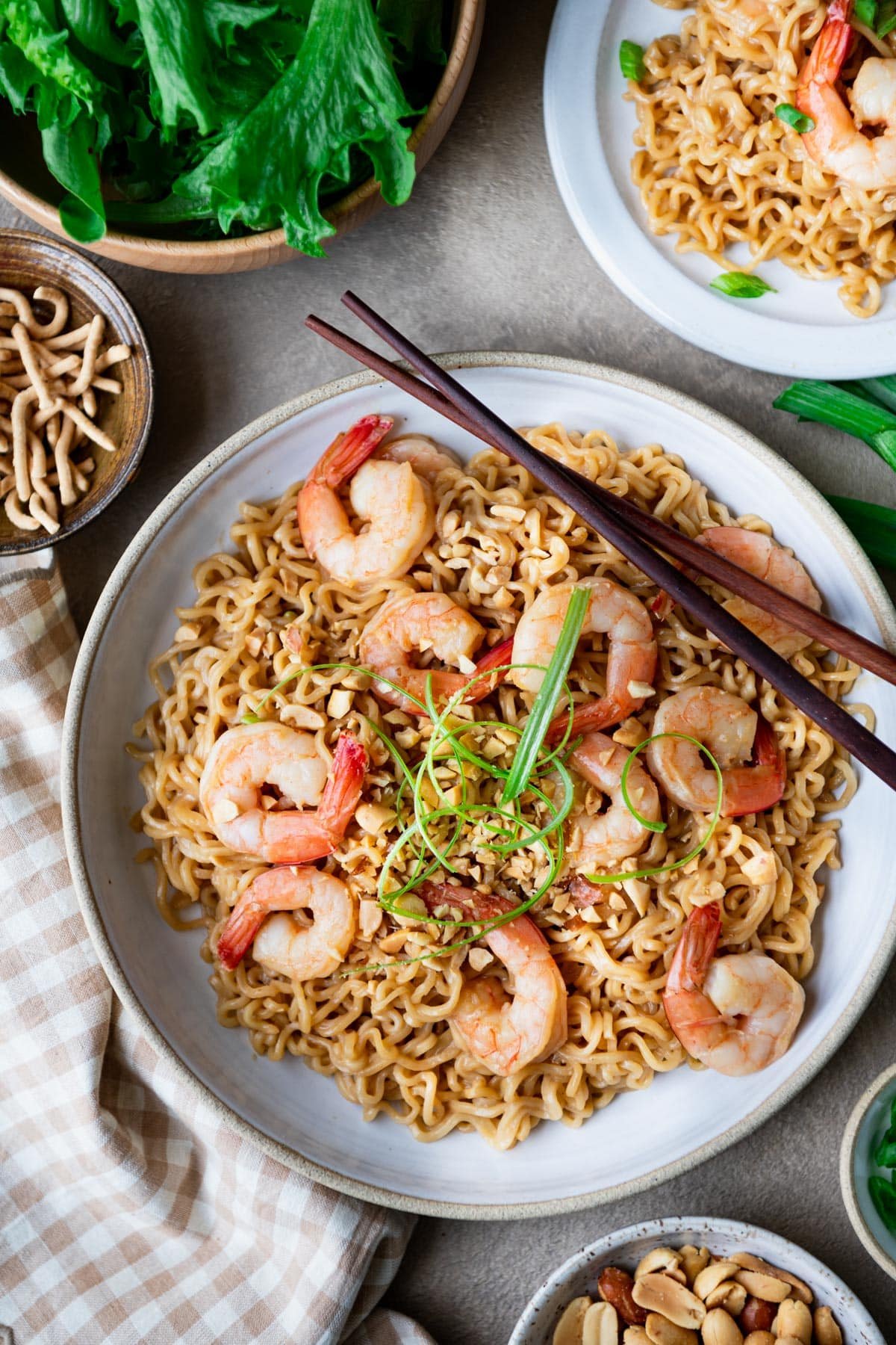 Chopsticks on a bowl of shrimp ramen with green onions and chopped peanuts on top.