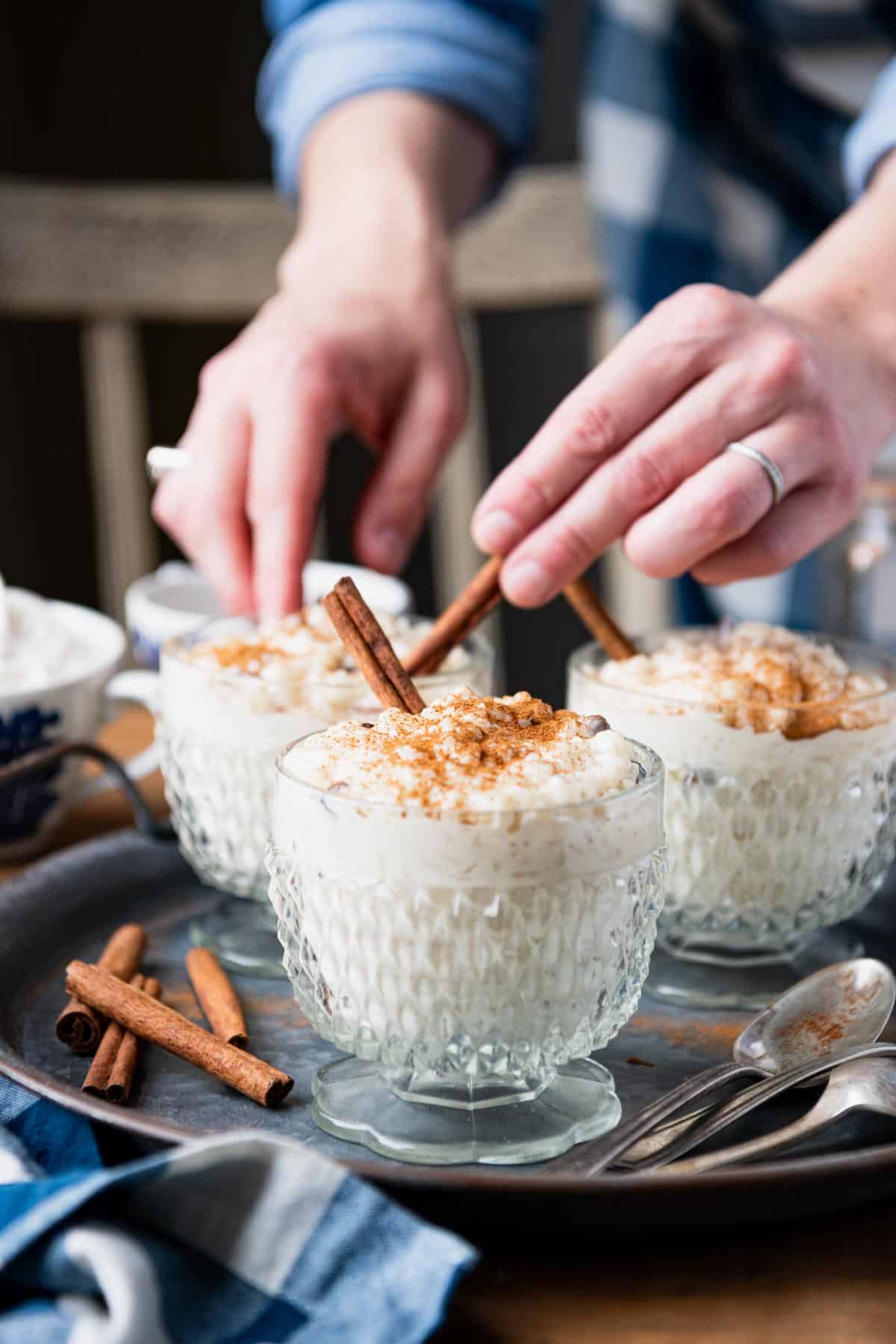 Hand serving rice pudding with cinnamon sticks.