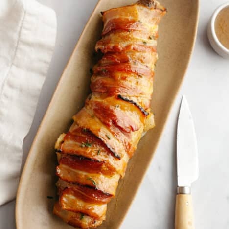 Square overhead shot of a bacon wrapped pork tenderloin on a serving platter.
