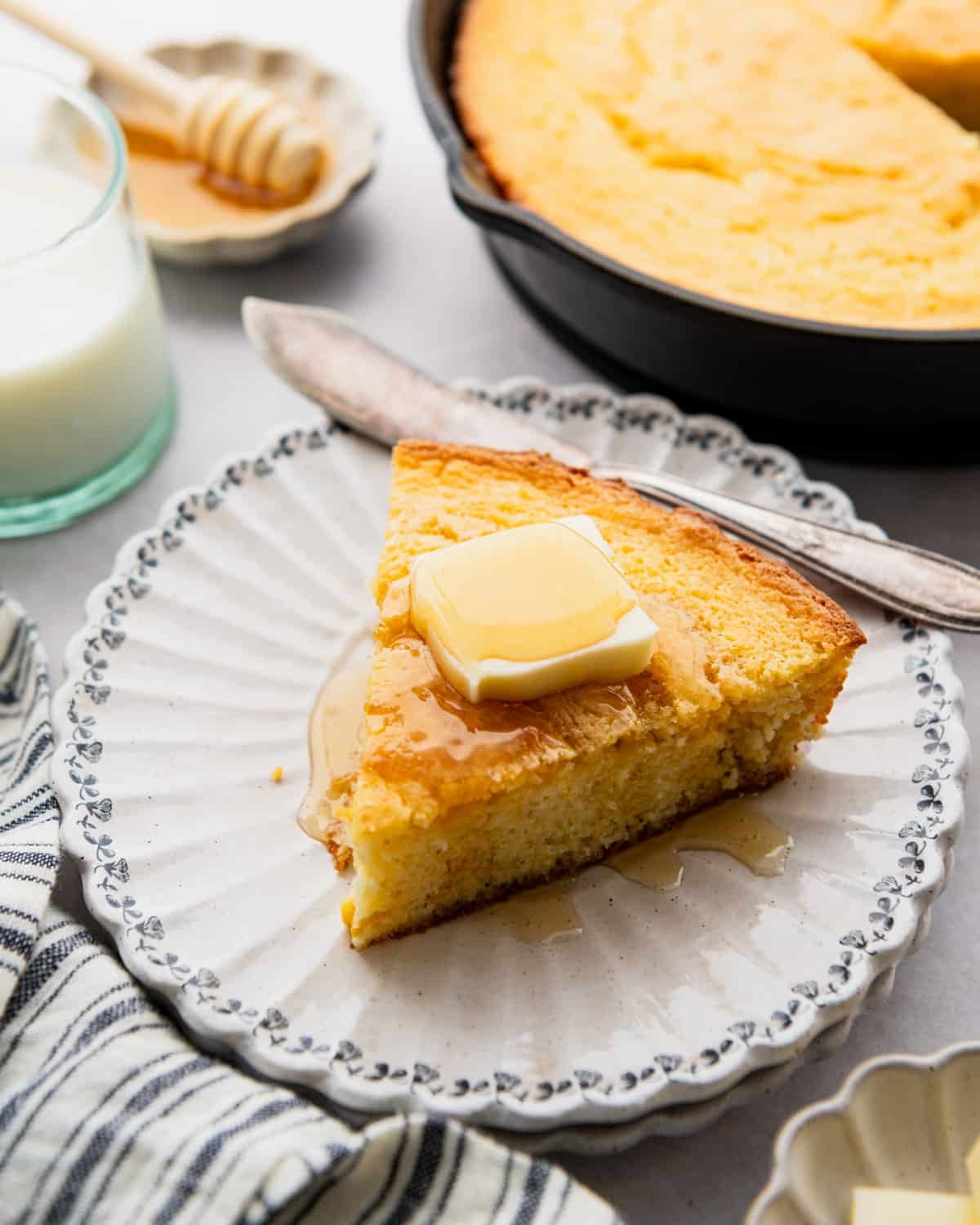 Front shot of a slice of sour cream cornbread on a blue and white plate with butter and honey on top.