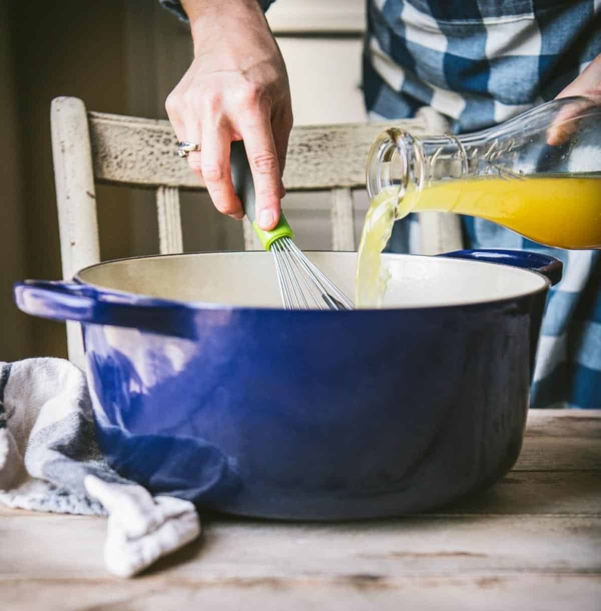 Pouring broth into a blue dutch oven
