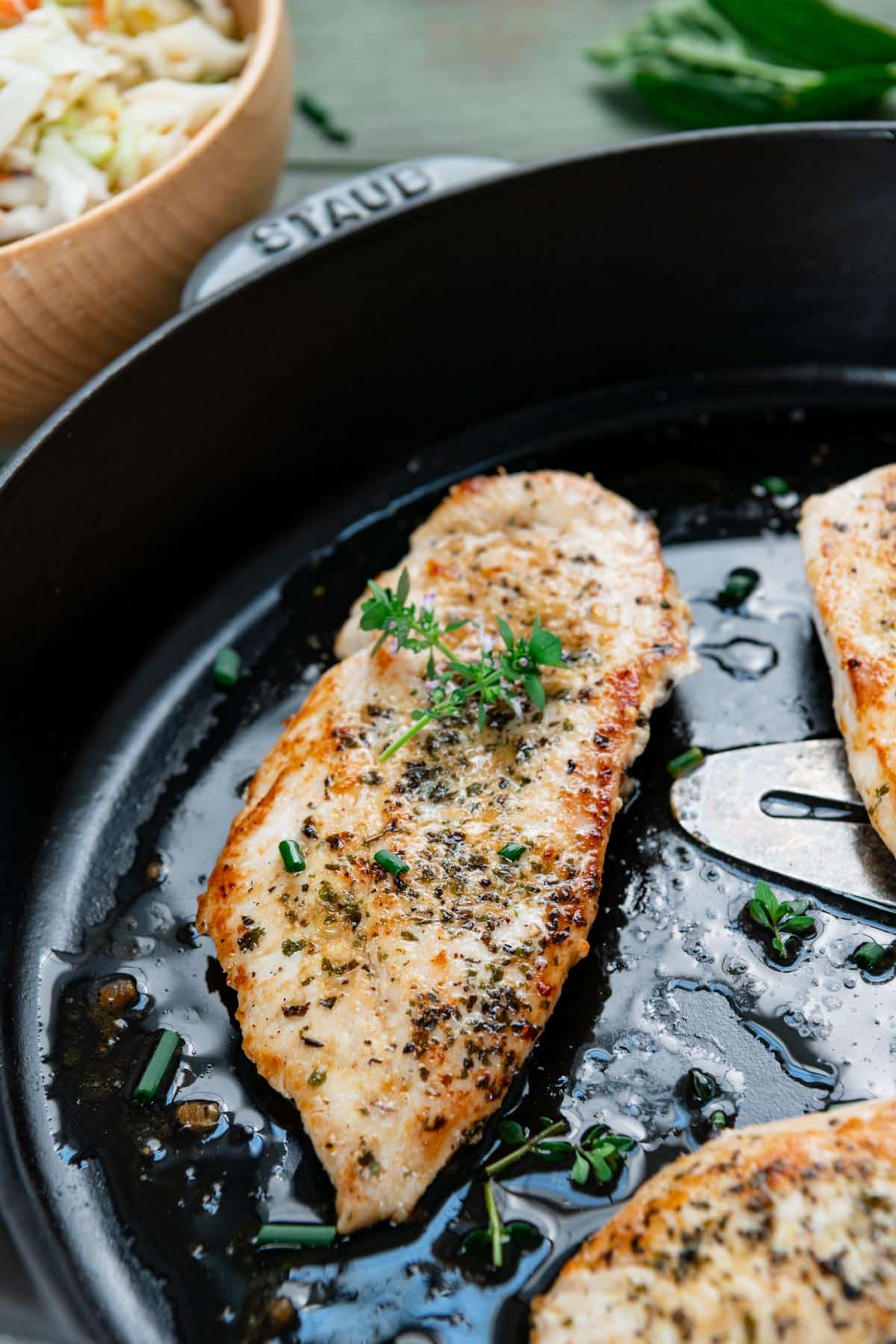 Side shot of cast iron chicken breast in a pan with fresh herbs.