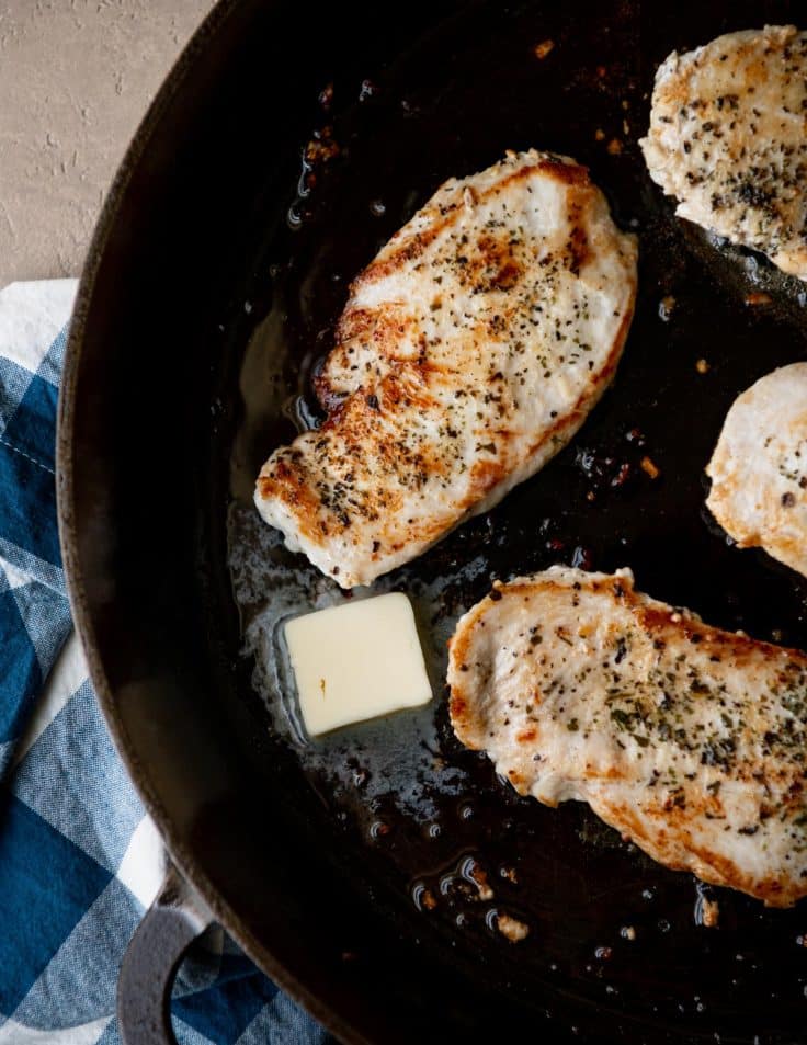 Basting chicken breast with melted butter in a cast iron skillet.