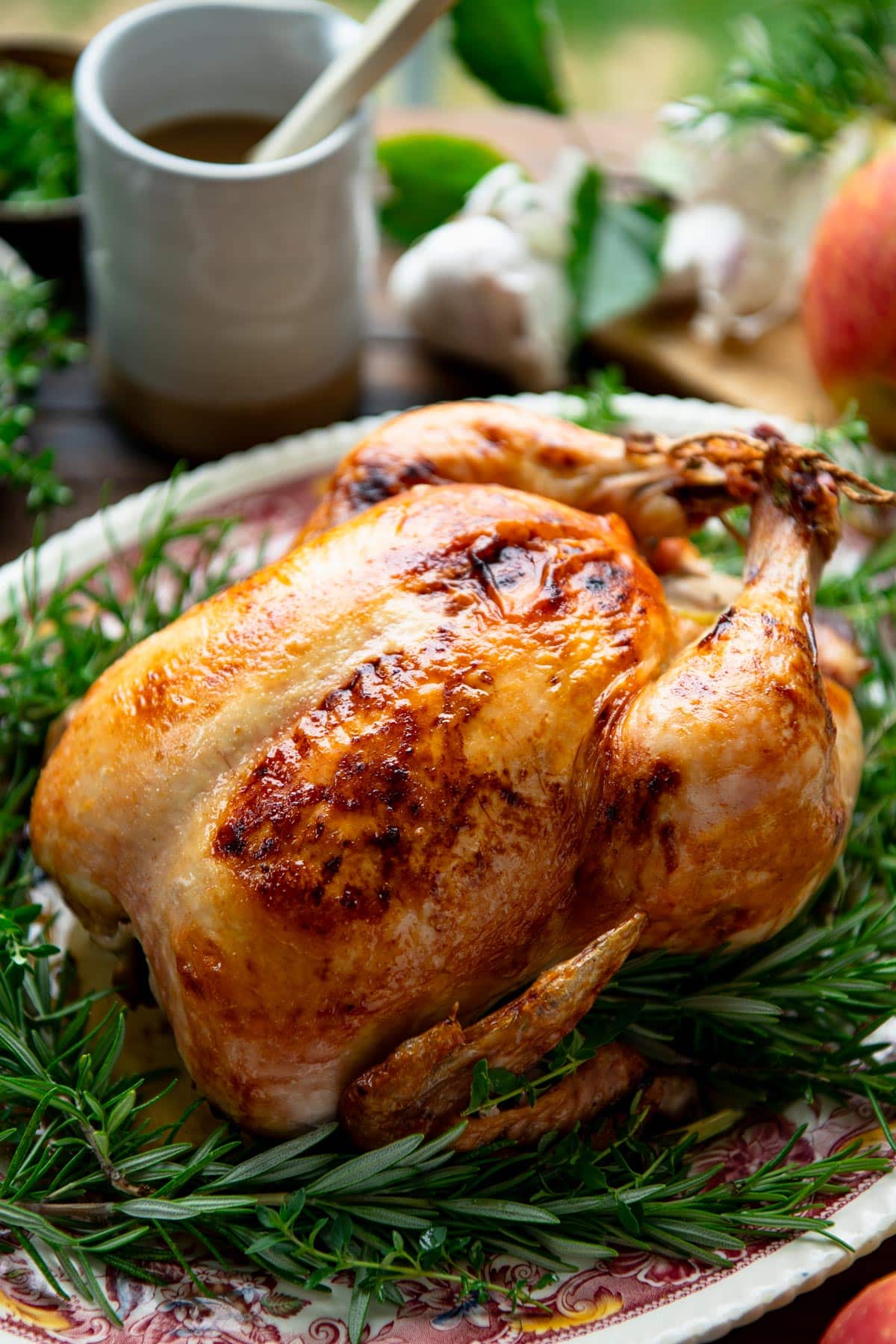 Golden roast chicken on a serving platter with fresh herbs.