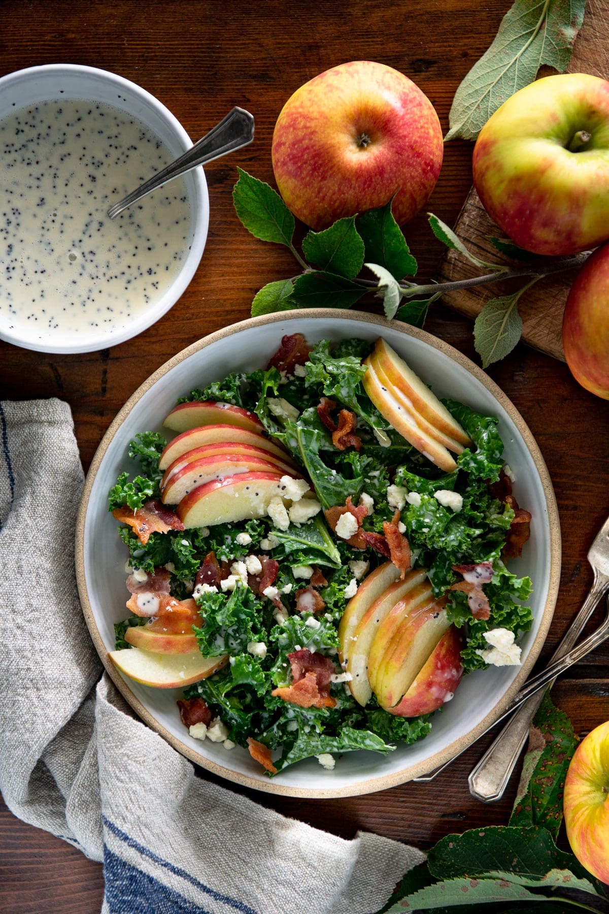 Overhead shot of kale apple salad on a table with homemade creamy poppy seed dressing on the side.