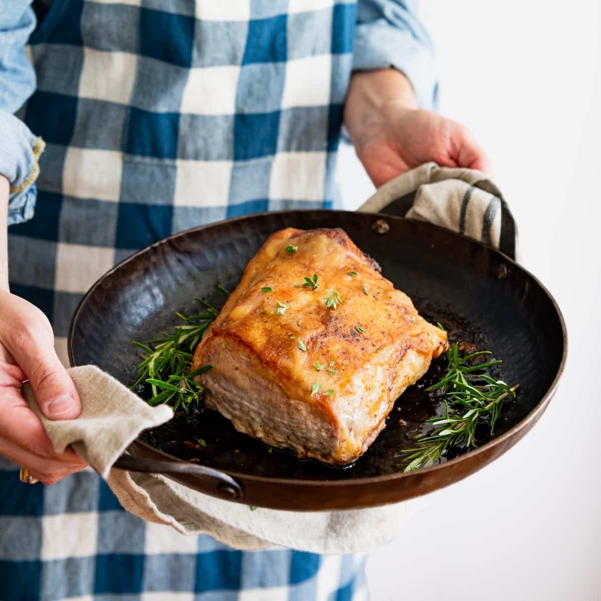Square side shot of hands holding an oven roasted pork loin in a cast iron skillet.