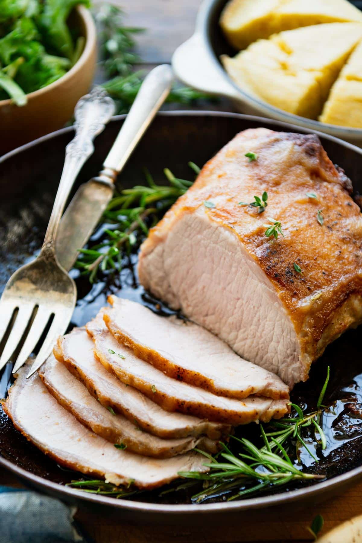 Close up shot of a oven roasted pork loin roast sliced and served with fresh rosemary.