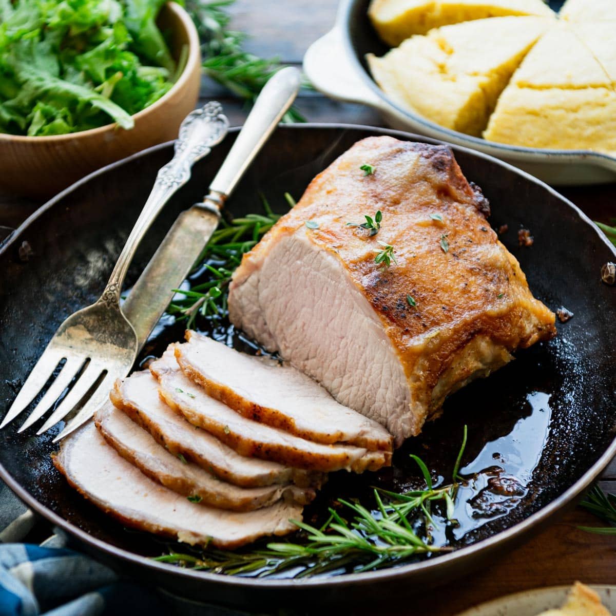 Square side shot of oven roasted pork loin served with salad and cornbread.