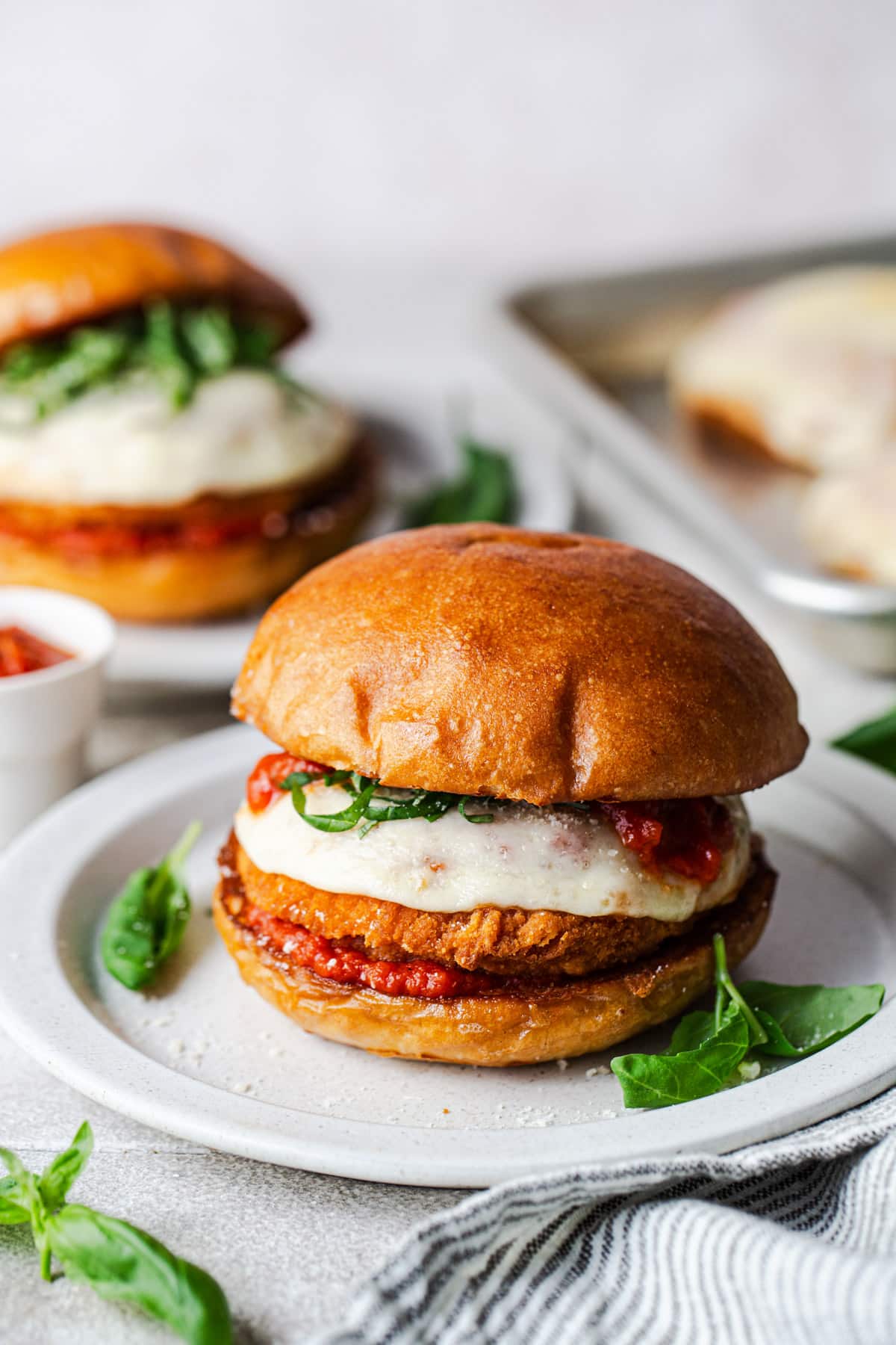 Side shot of an easy chicken Parmesan sandwich on a white plate with fresh basil for garnish.