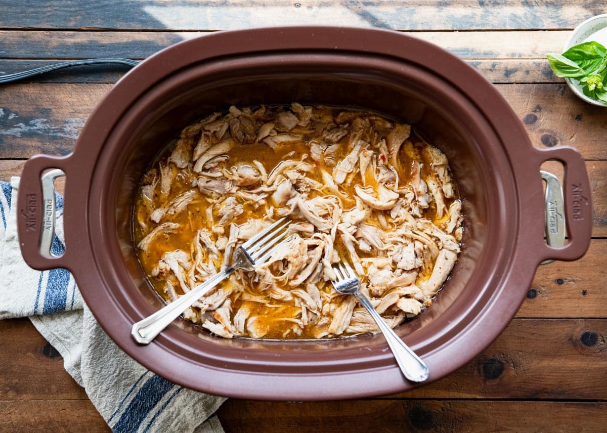 Shredded chicken in a slow cooker with two forks.