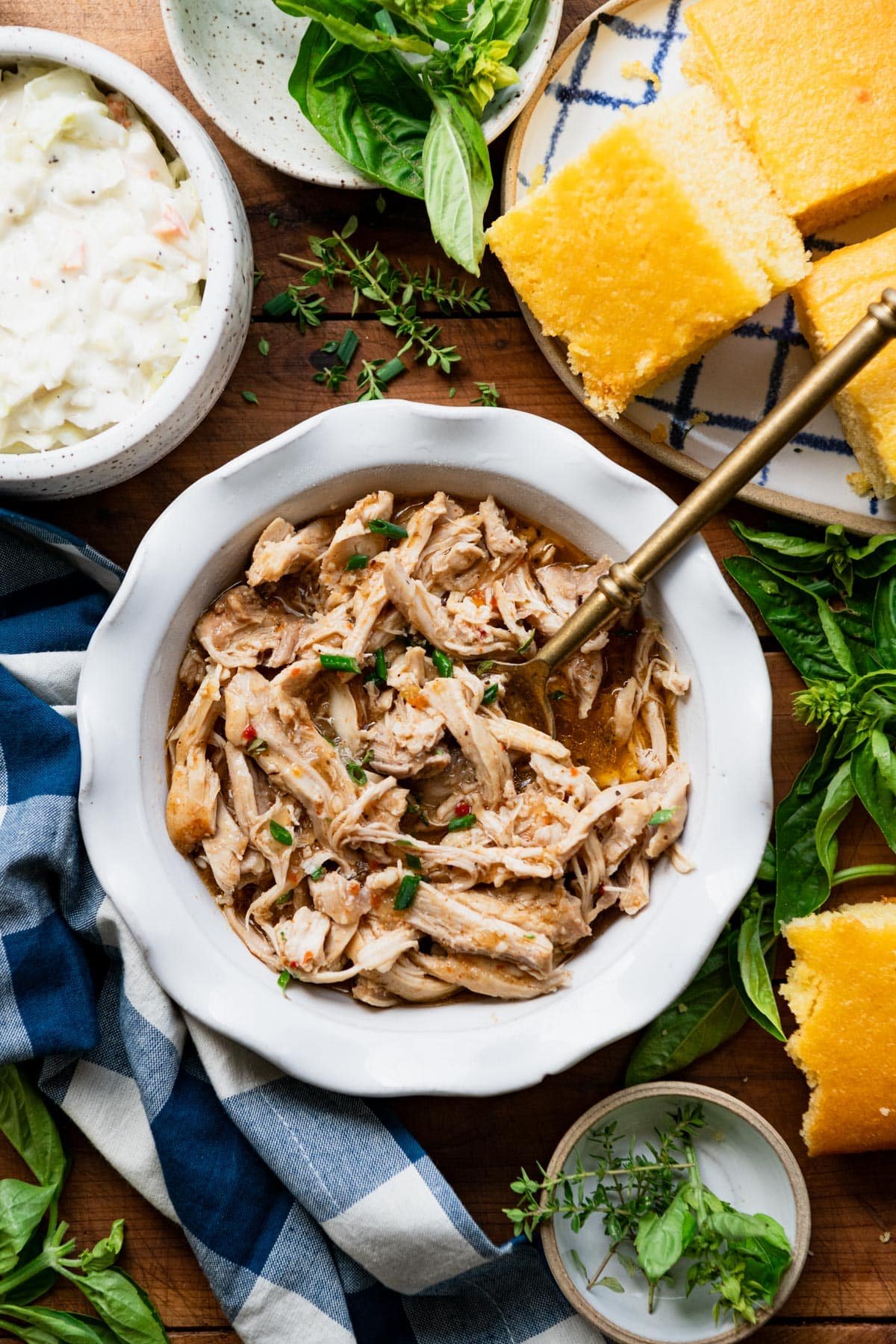 Overhead image of a serving bowl of 3-ingredient crock pot pulled chicken on a wooden dinner table.