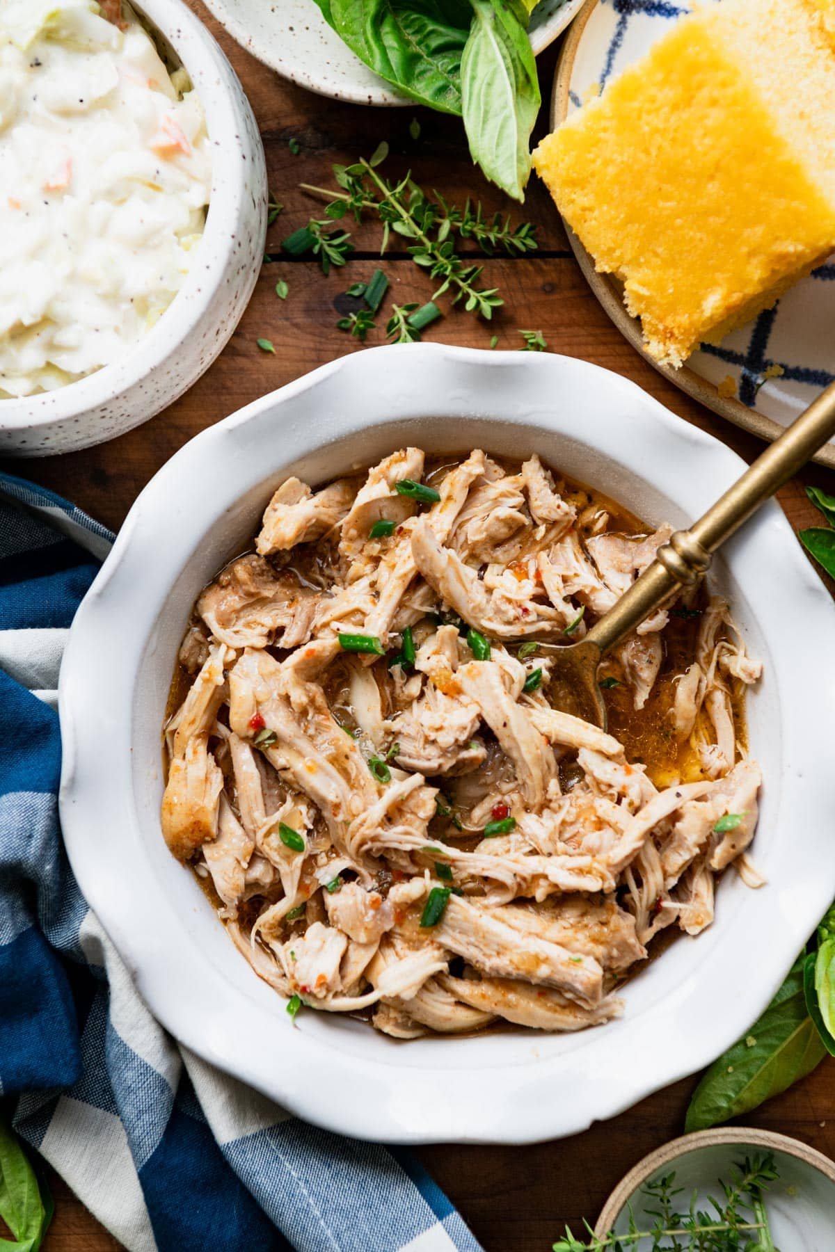 Close overhead shot of a bowl of crock pot pulled chicken with a gold serving spoon.