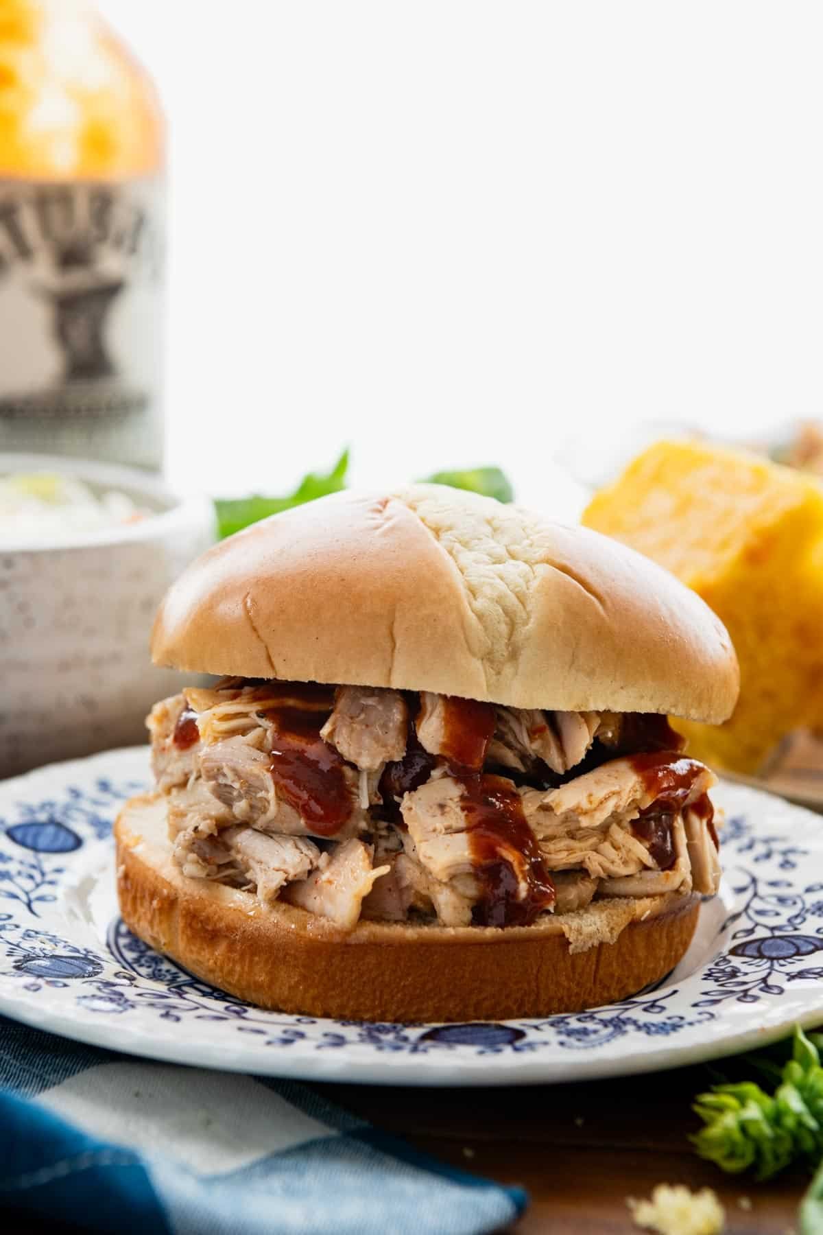Side shot of 3-ingredient crock pot pulled chicken on a sandwich on a blue and white plate.