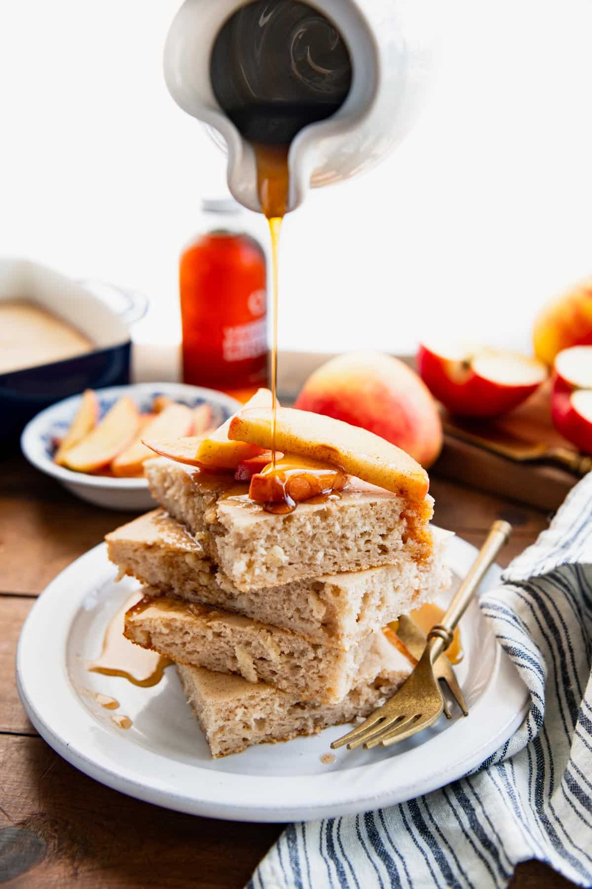 Pouring maple syrup on a plate of baked apple pancakes.