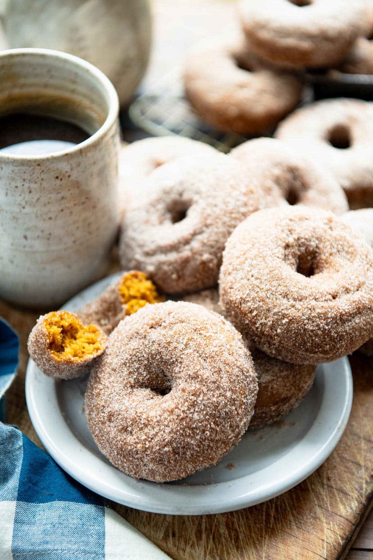 Side shot of pumpkin doughnuts on a white plate with a mug of coffee.