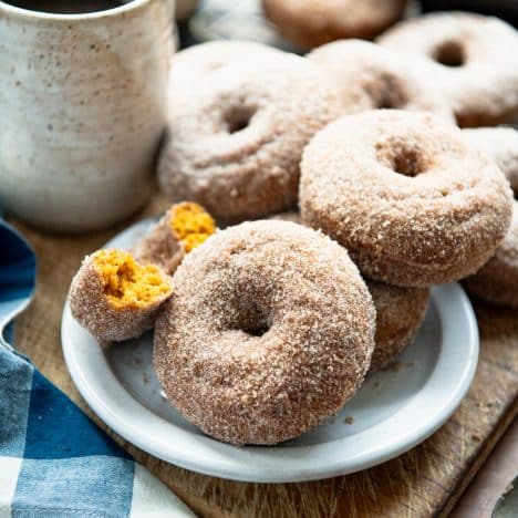 Square side shot of baked pumpkin donuts on a wooden table with a cup of coffee