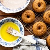 Process shot showing how to coat pumpkin donuts in melted butter and cinnamon sugar.