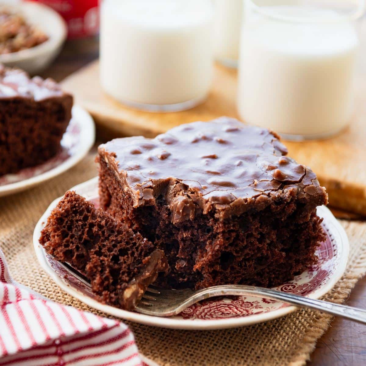 Coca cola cake recipe served on a plate with glasses of milk on the side.