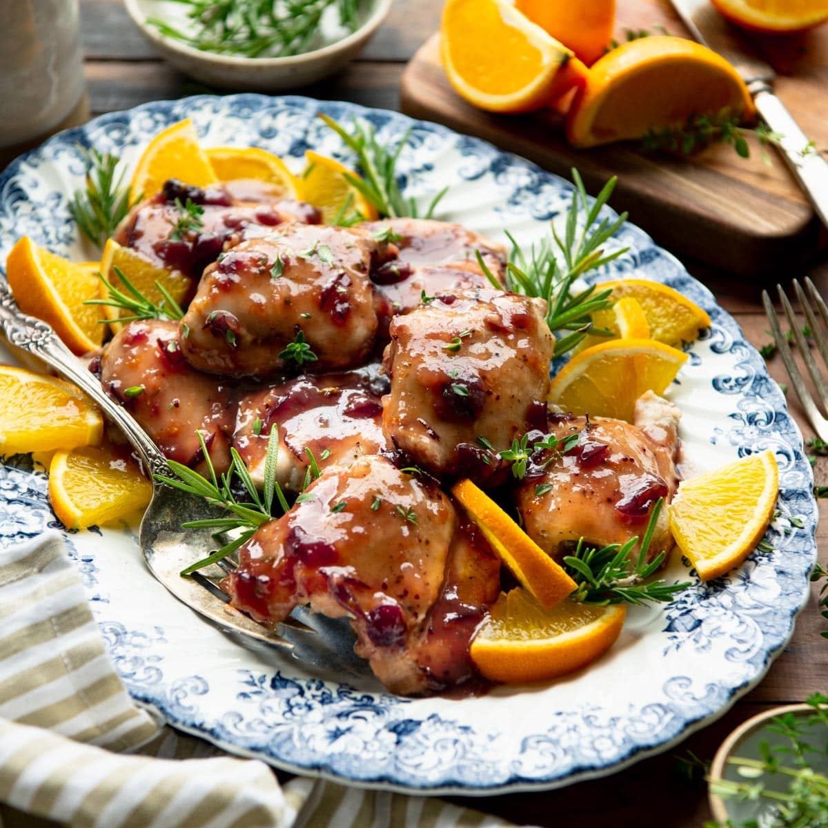 Square side shot of crock pot cranberry chicken on a blue and white platter.