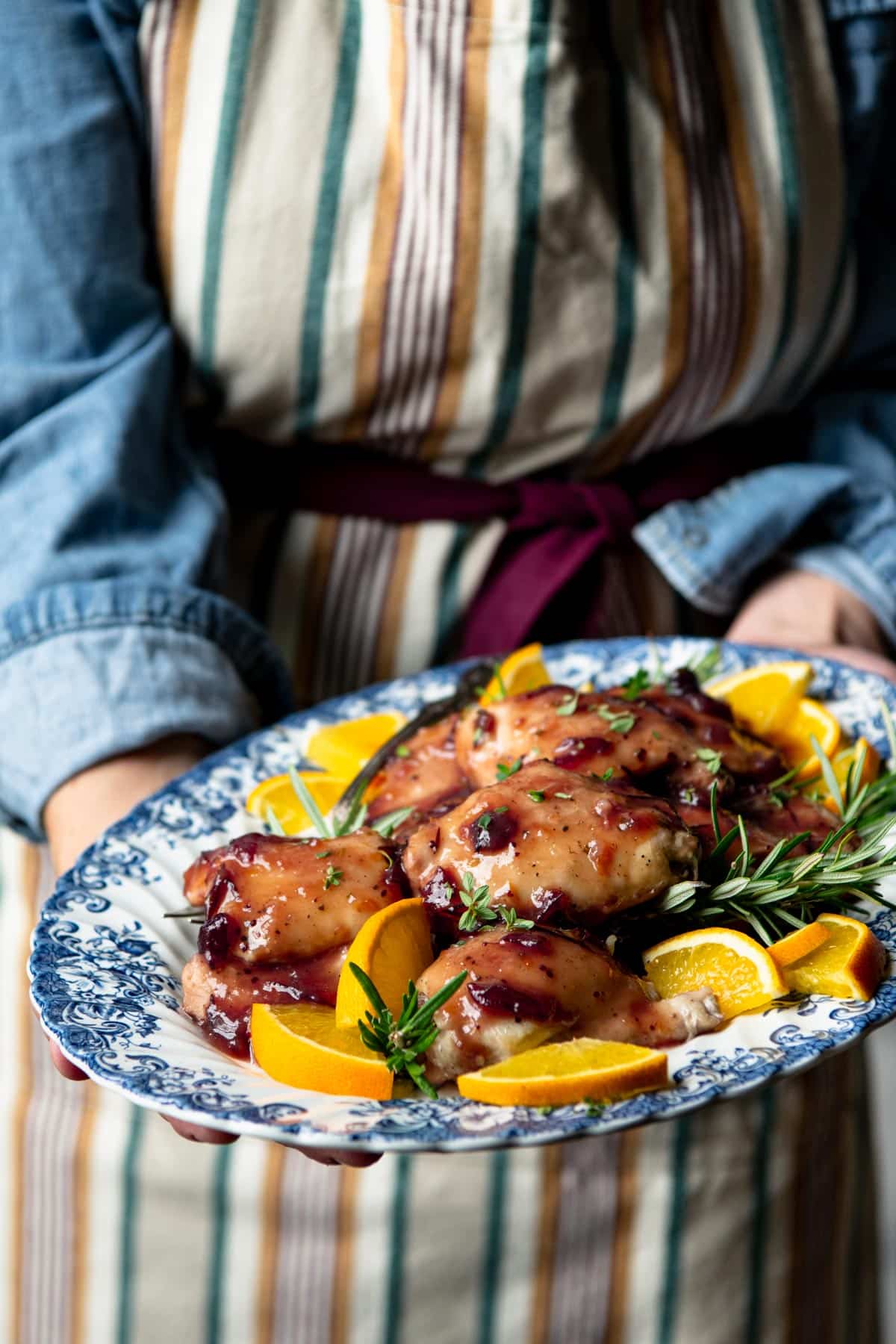 Hands holding a platter of cranberry chicken.