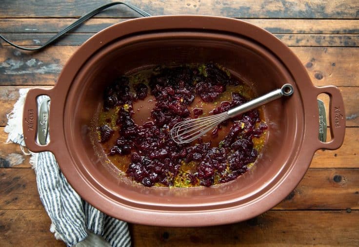 Whisking cranberry sauce with other sauce ingredients in a slow cooker.