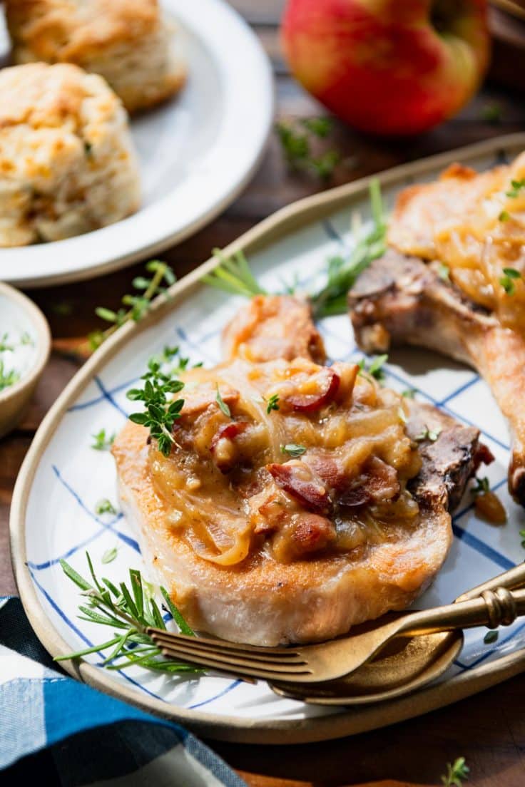 Close up side shot of crock pot pork chops on a platter with bacon and onion gravy.