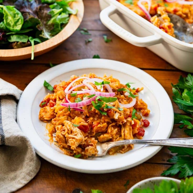 Square side shot of chicken fajita casserole with rice on a white plate.