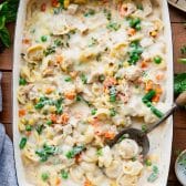 Baked tortellini alfredo in a white dish with a serving spoon.