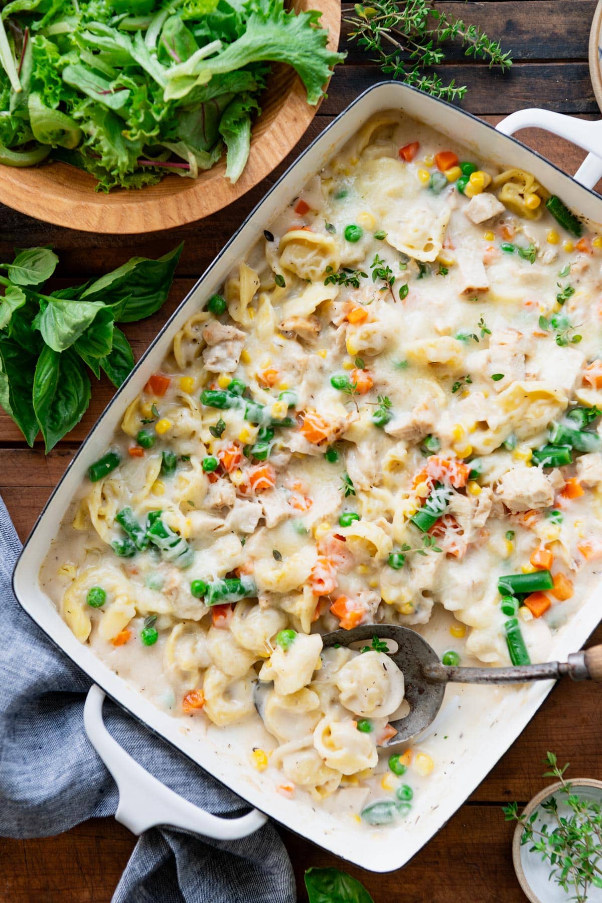 Overhead shot of baked tortellini alfredo in a white pan on a wooden table with a side salad.