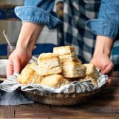 Square side shot of hands serving a tray of homemade buttermilk biscuits with flaky layers.