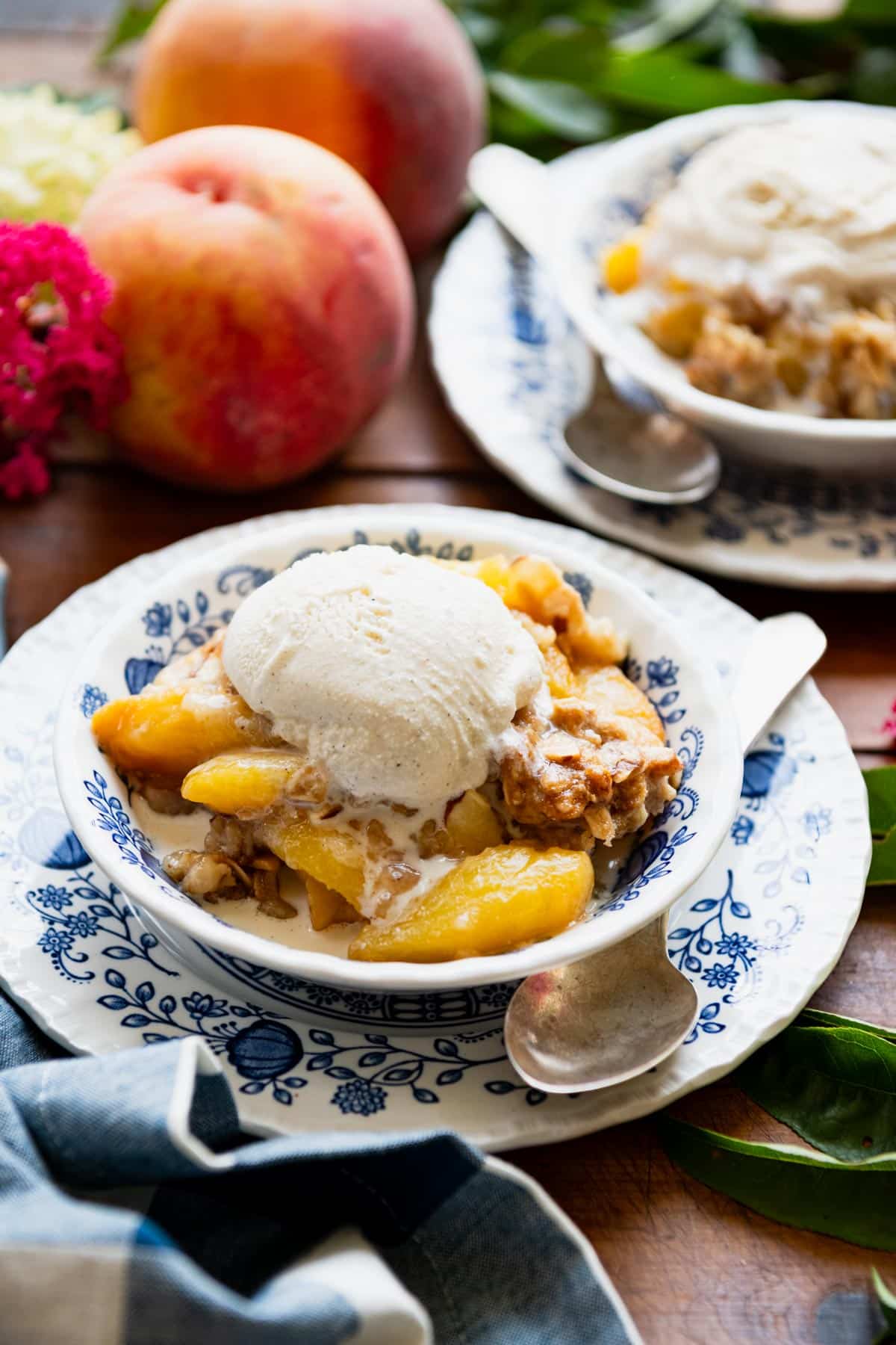 Close up side shot of peach crisp in a bowl with ice cream on top.
