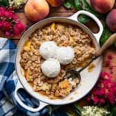 Square overhead shot of an easy peach crisp recipe baked in a white cast iron skillet.
