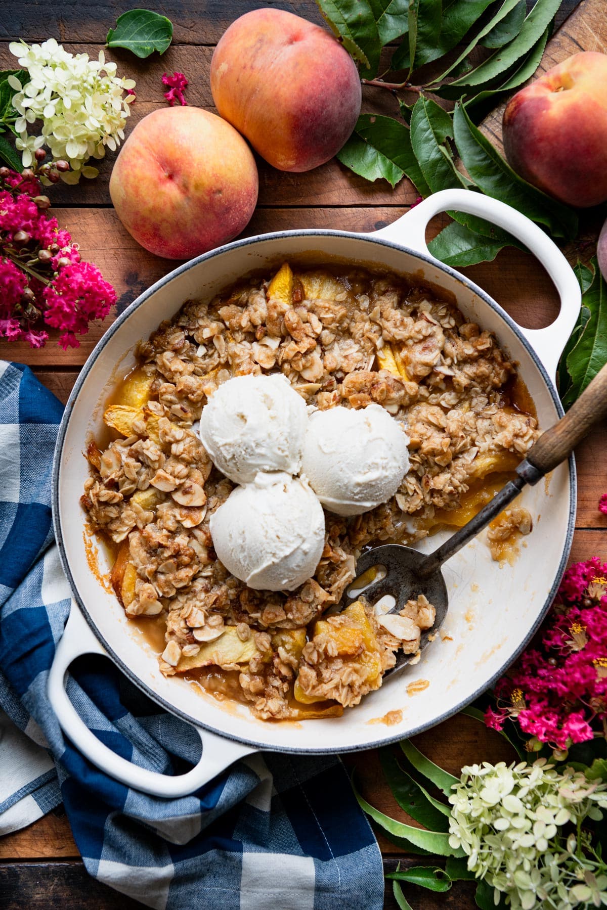 Warm skillet of the best peach crisp recipe on a table with ice cream on top.