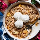 White cast iron skillet full of an easy peach crisp recipe and topped with three scoops of vanilla ice cream.