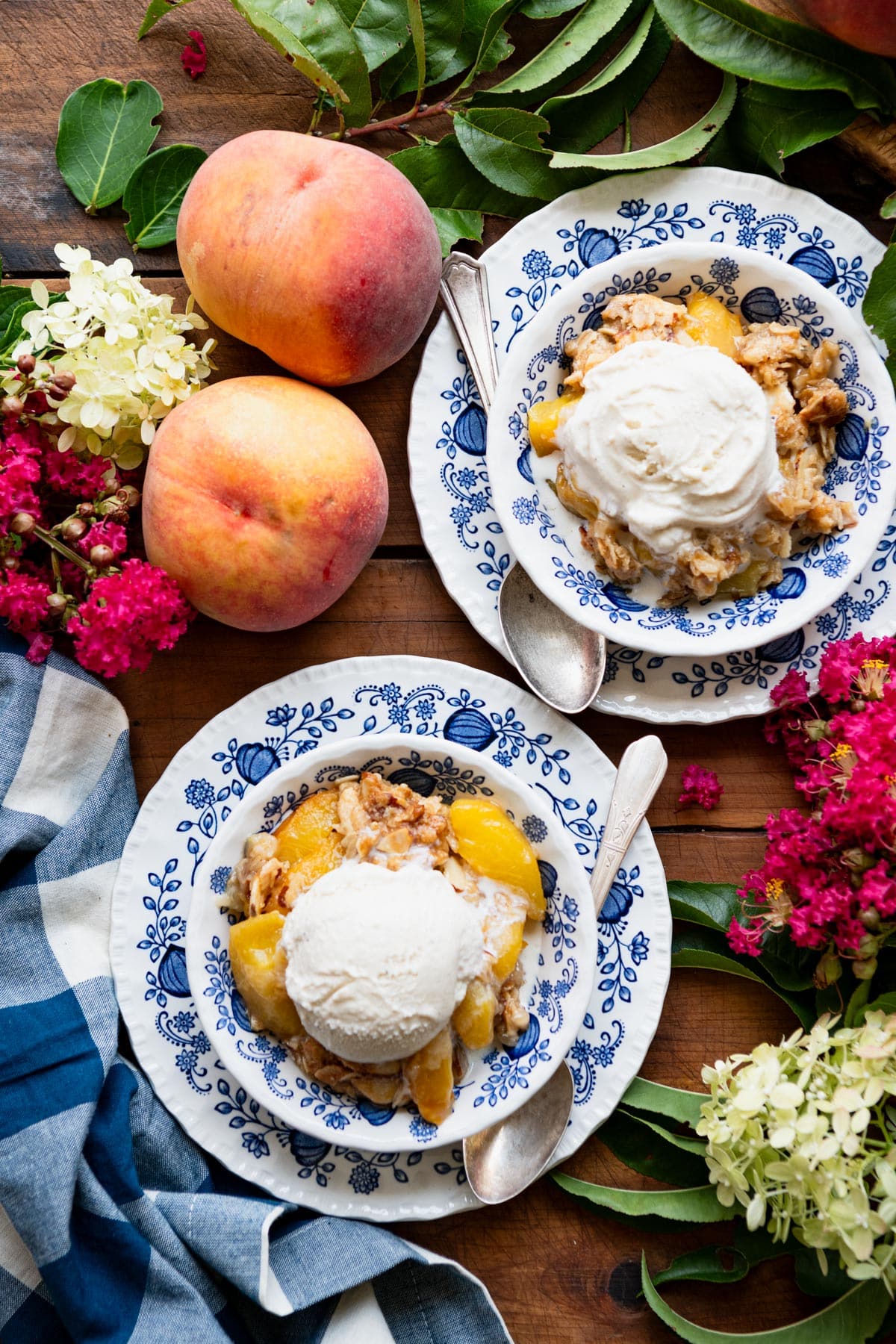 Two bowls of easy peach crisp on a wooden table with vanilla ice cream on top.