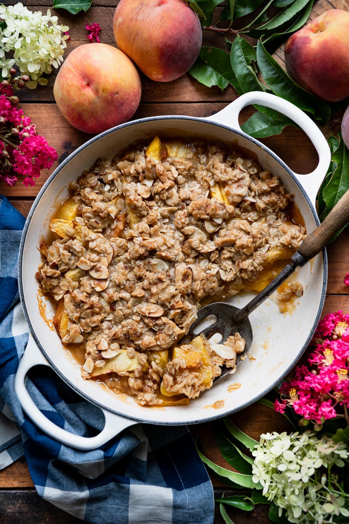 Peach crisp in a cast iron skillet on a wooden table with flowers around the border.