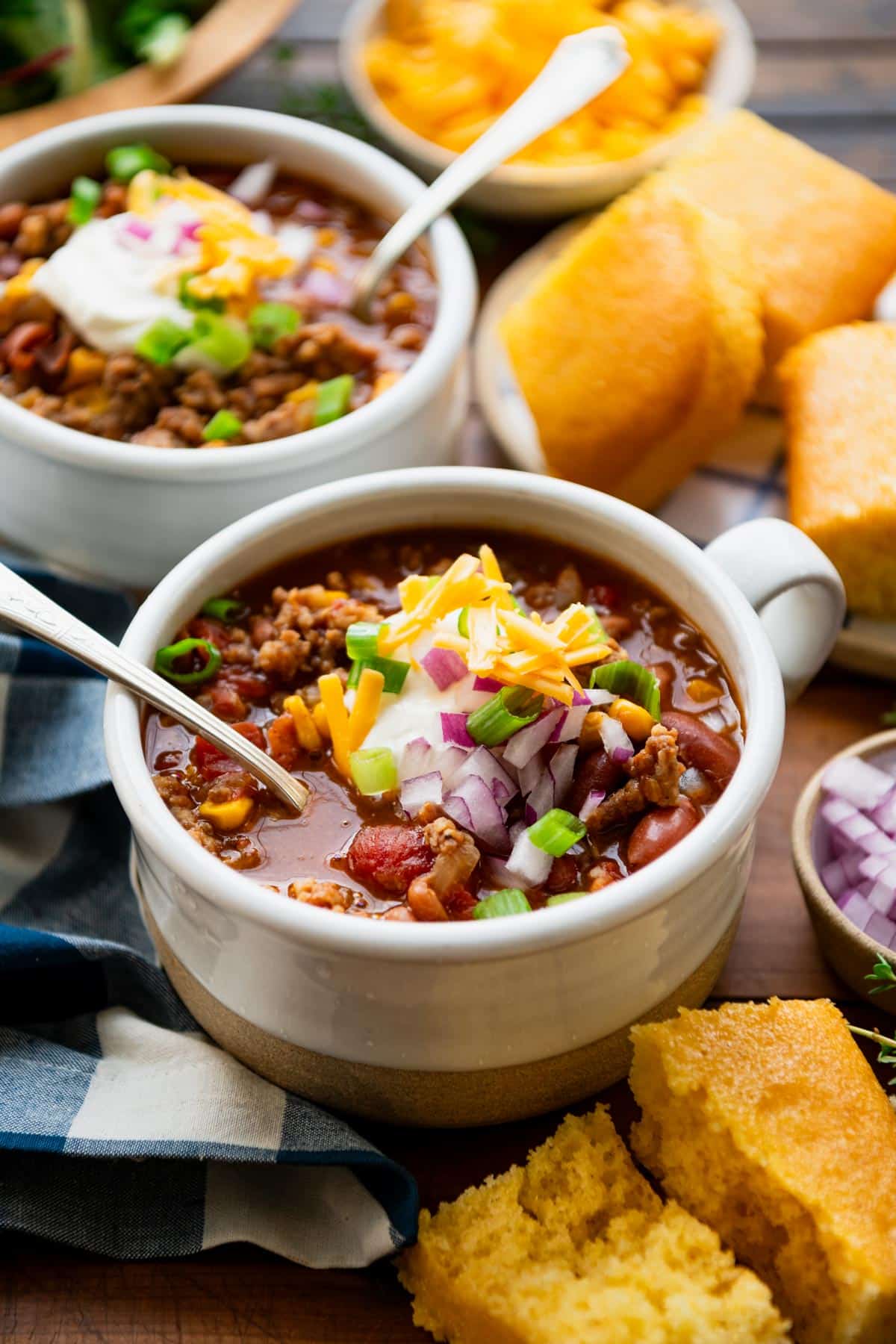 Spoon in a bowl of ground pork chili with cornbread on the side.