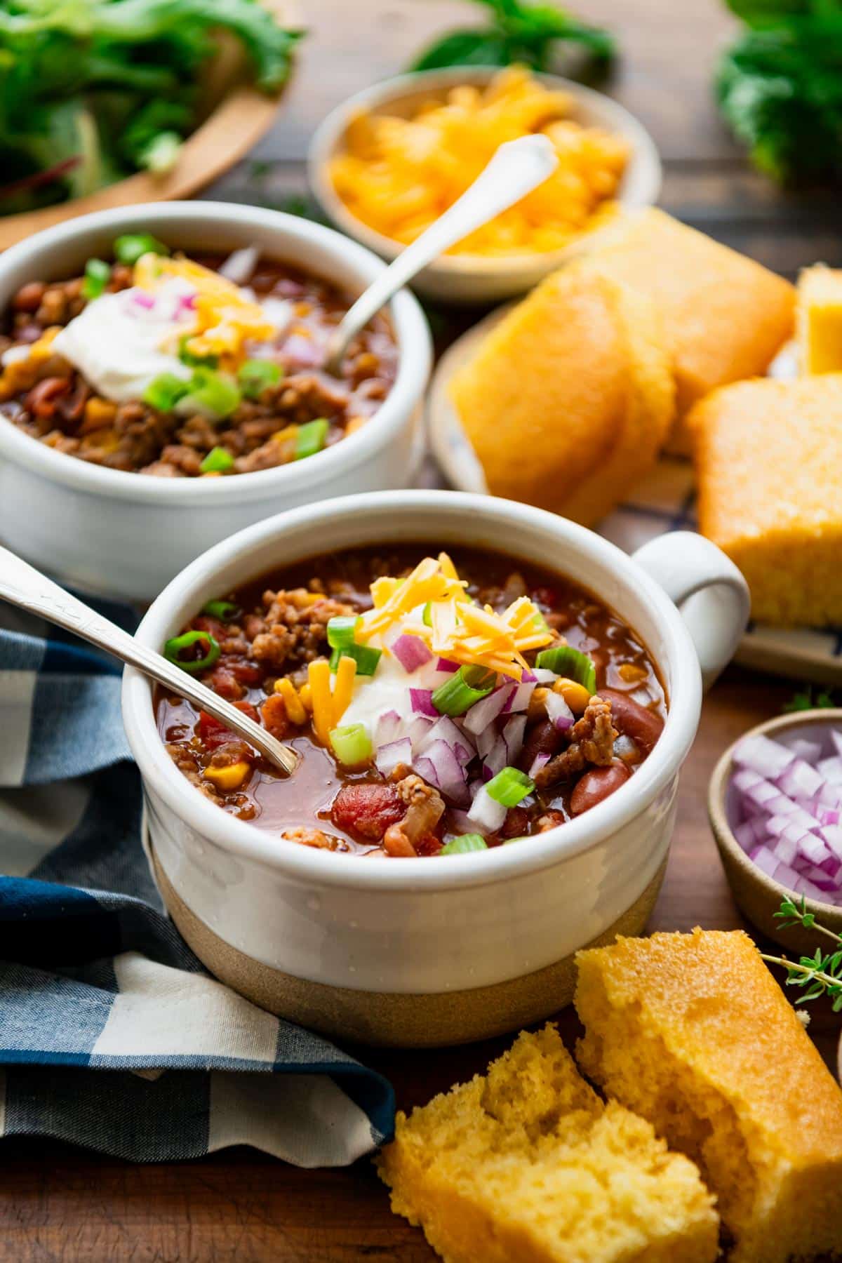 Cornbread and bowls of pork chili on a wooden table.