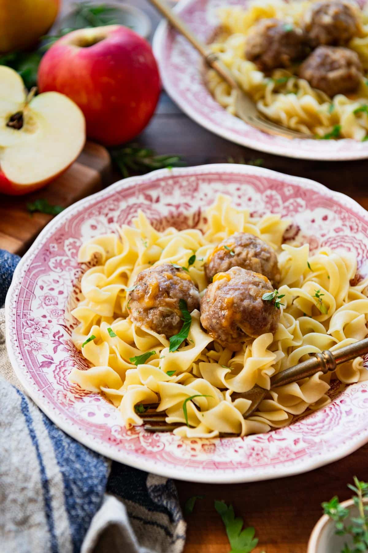 Fork in a bowl of buttered egg noodles with pork sausage meatballs on top.