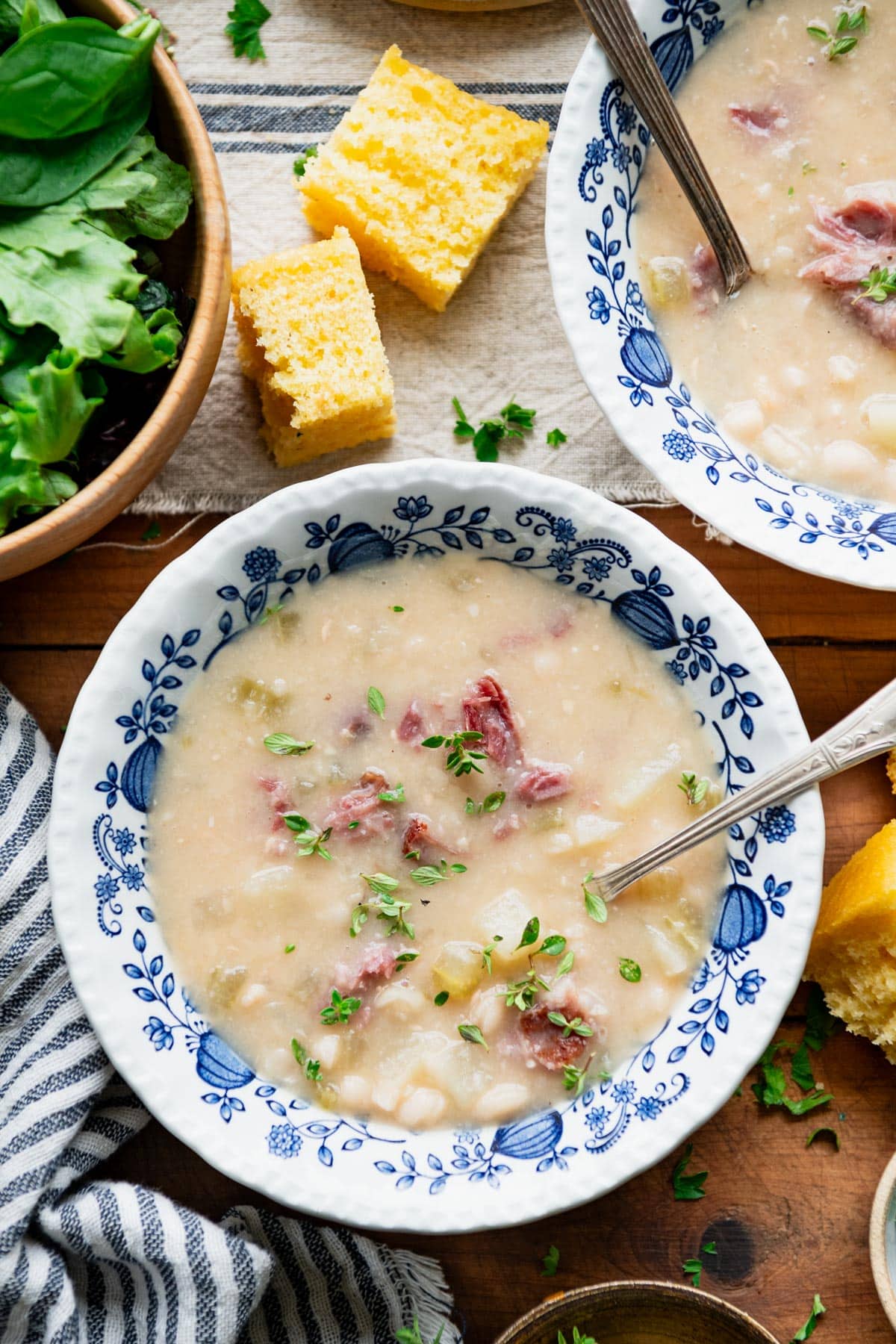 Overhead image of ham bean soup in a blue and white bowl with a side of cornbread.