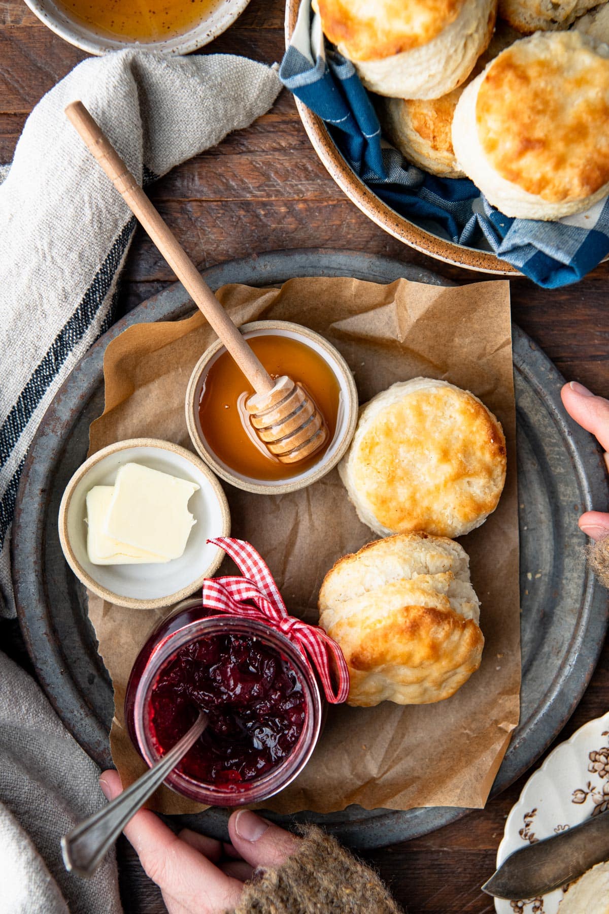 Hands holding a plate with two buttermilk biscuits and honey, butter, and jam.