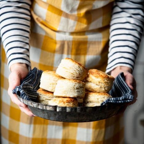 Square side shot of a woman in an apron holding a bowl of 3 ingredient biscuits.