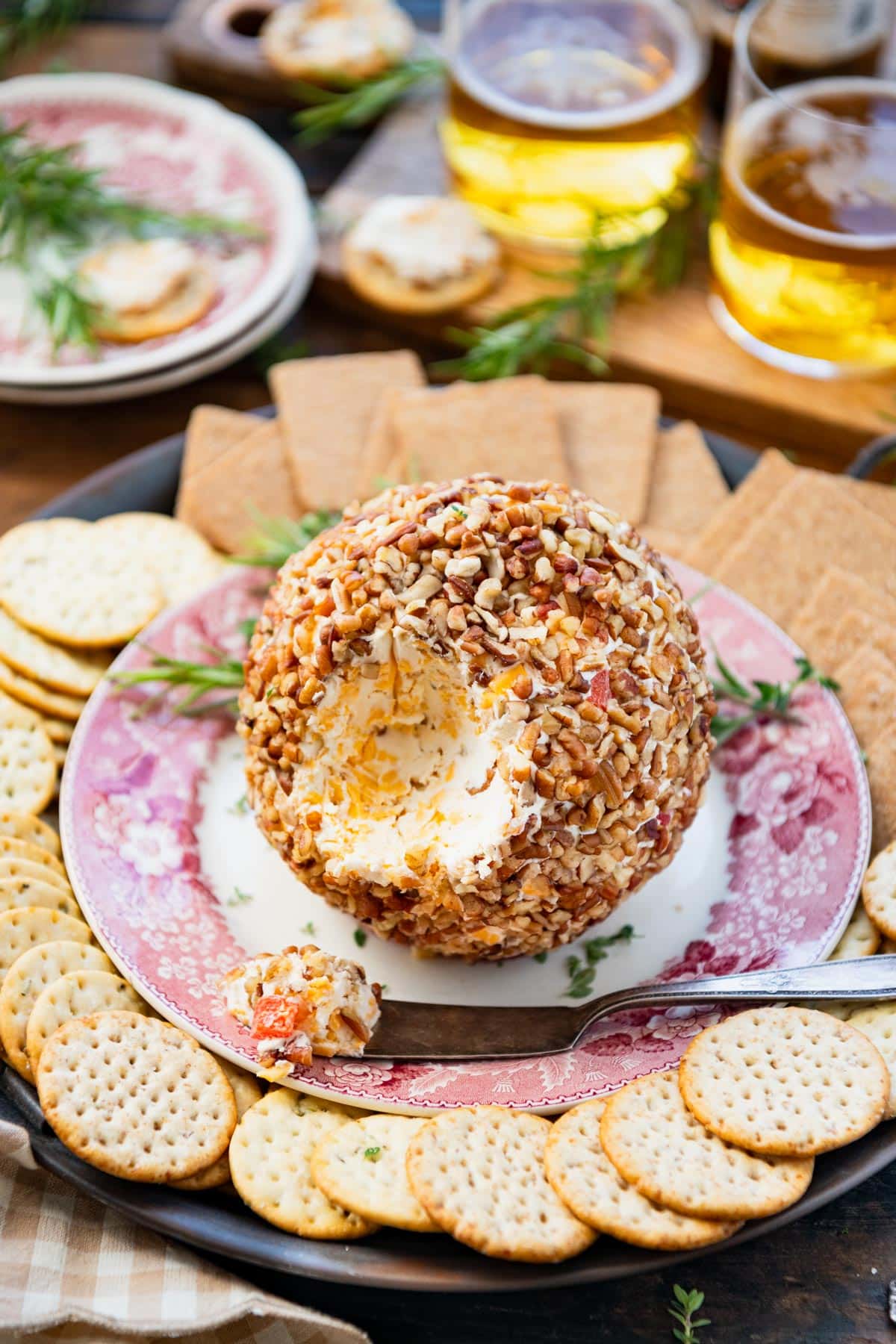 Front shot of a table of appetizers including glasses of beer, crackers, and a classic cheese ball.