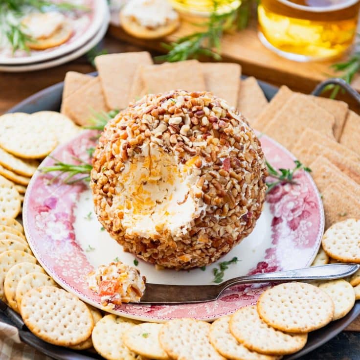 Square side shot of an easy cheese ball recipe with herbs and rackers on a table.