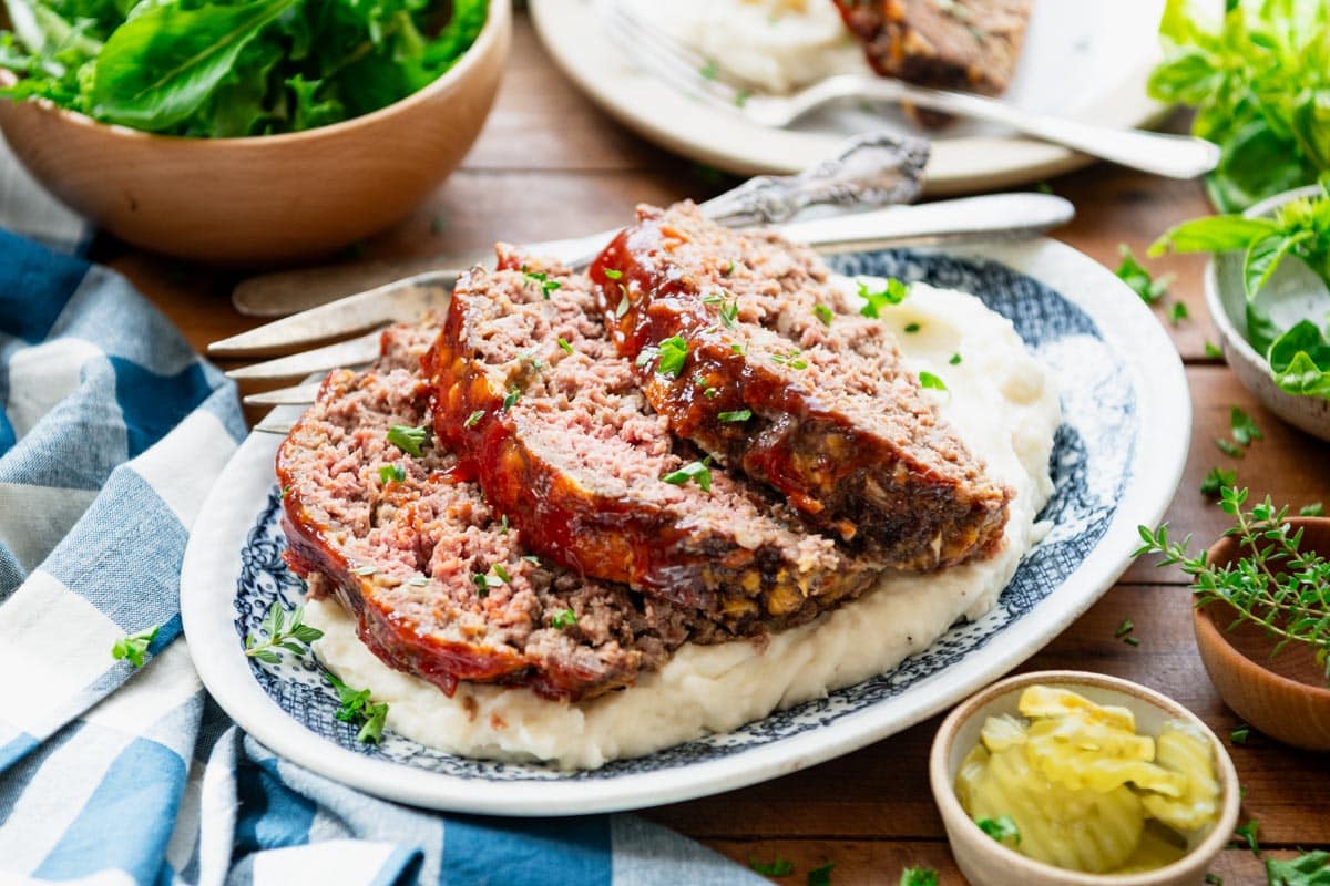 Horizontal image of a platter of sliced meatloaf with cheese and a side of mashed potatoes.