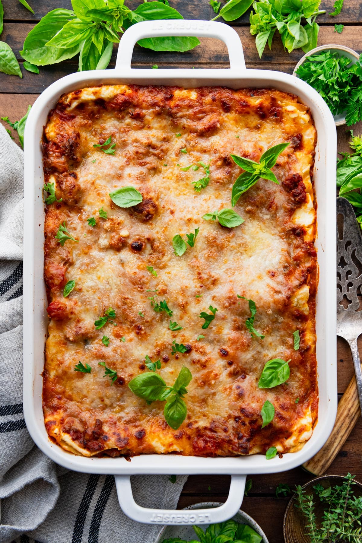 Pan of classic lasagna recipe in a white dish on a wooden table.