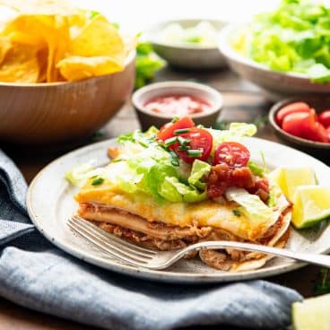 Square side shot of a simple chicken quesadilla casserole on a plate with a side of tortilla chips.