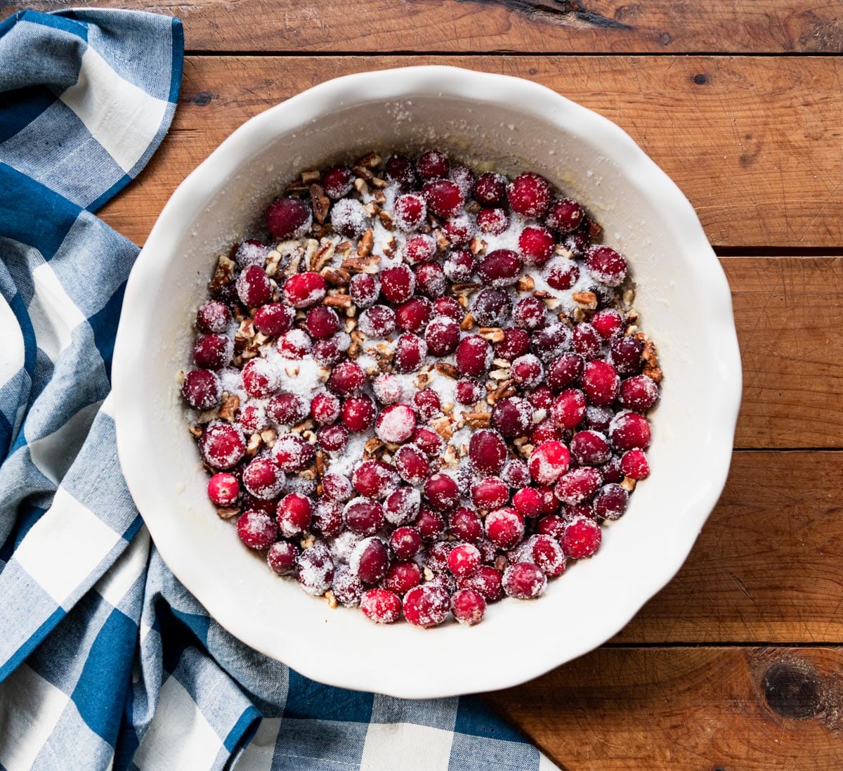 Cranberries pecans and sugar in the bottom of a white pie plate.