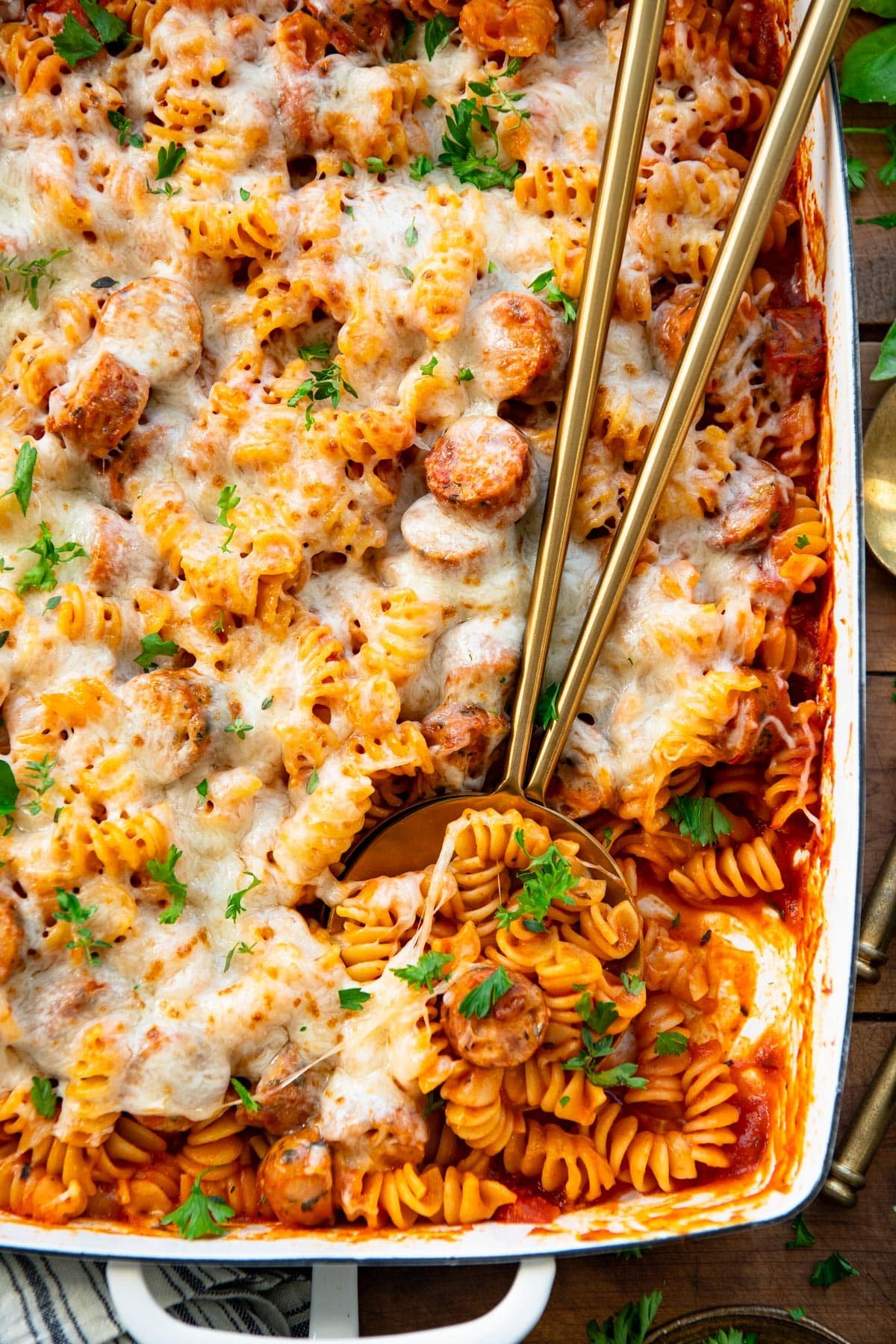 Close overhead shot of serving spoons in a dish of italian sausage pasta casserole.