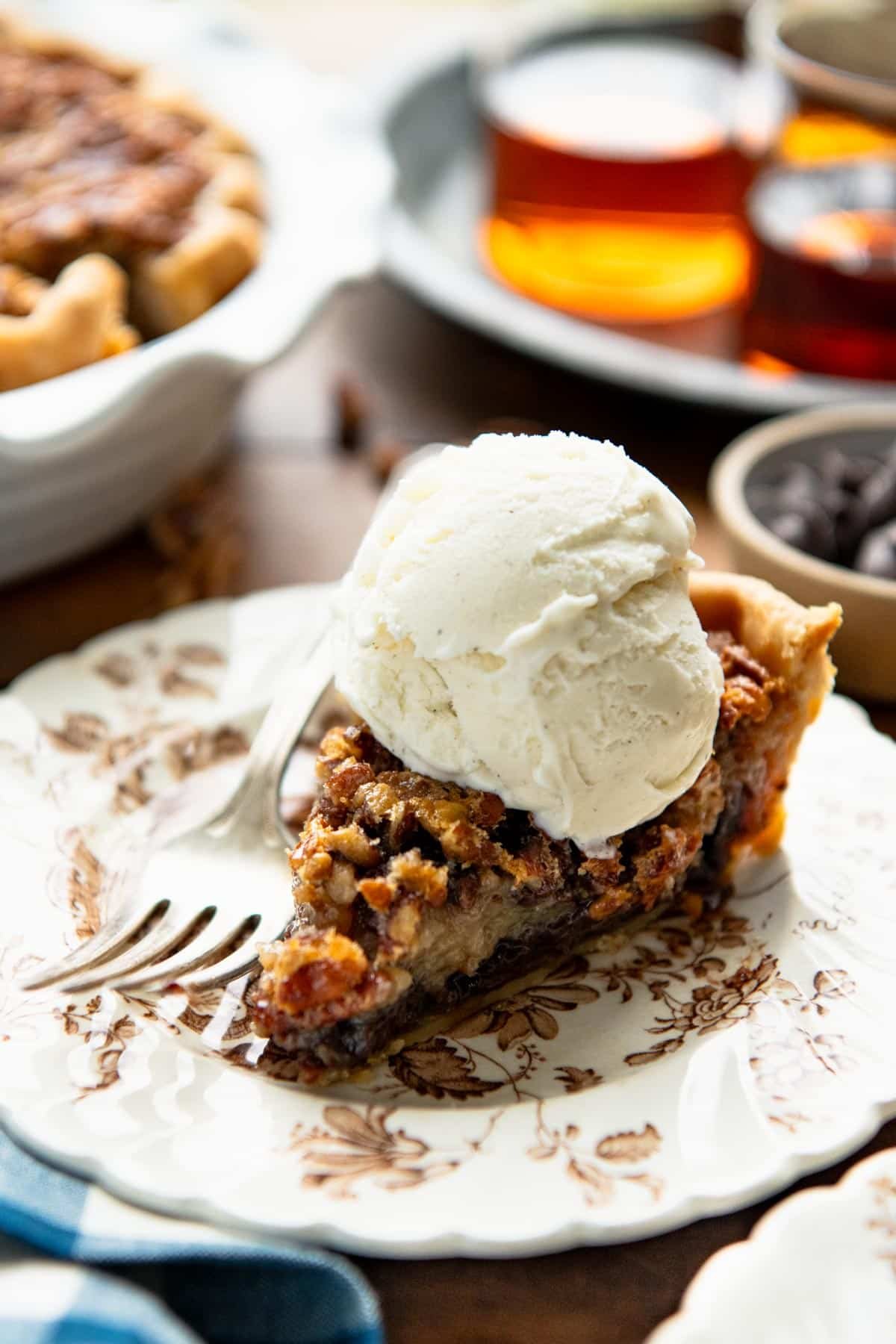 Side shot of pecan chocolate pie on a plate with a scoop of vanilla ice cream.